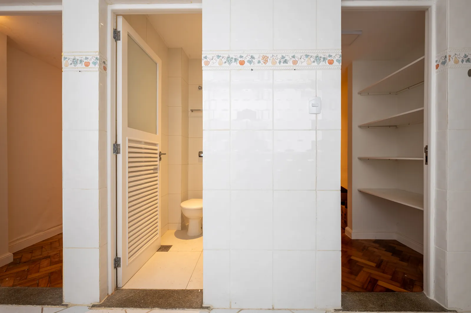 A bathroom with white tiling and fitted storage shelves