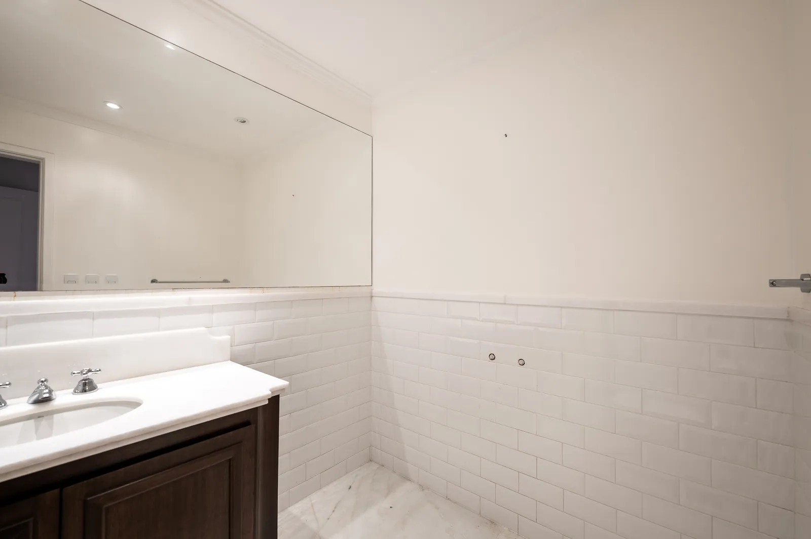 A bathroom with a dark-wood vanity, white tiling and a marble top